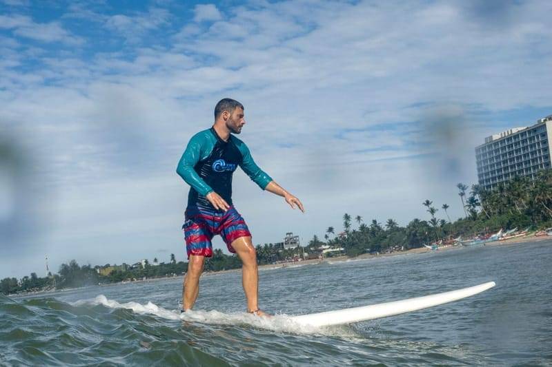 Ein Surfer fährt ein Longboard entlang der Küste von Weligama, Sri Lanka