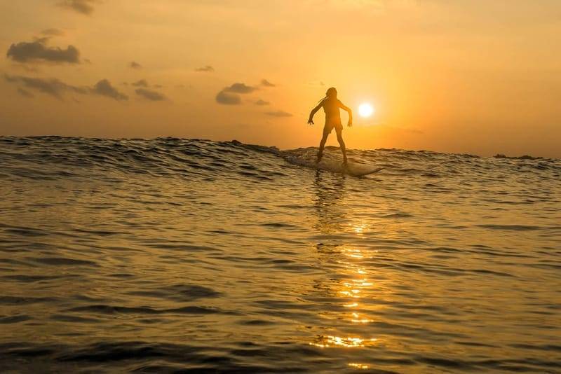 Silhouette eines Surfers auf einer Welle bei Sonnenuntergang vor der Südküste Sri Lankas