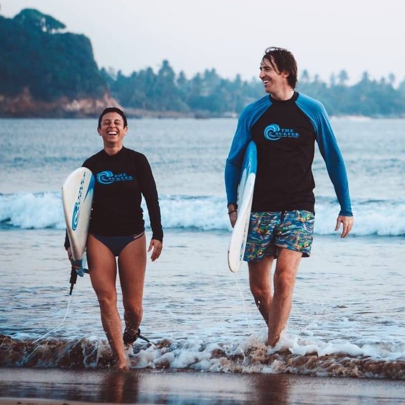 Zwei Gäste in Lycras von The Surfer kommen mit ihren Boards aus dem Wasser, Weligama