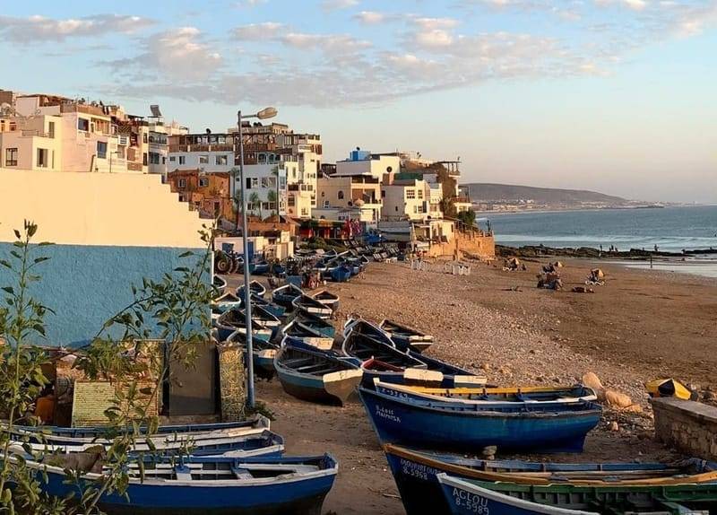 Blue fishing boats on the beach below a hillside village on Morocco’s Atlantic surf coast near Tamraght