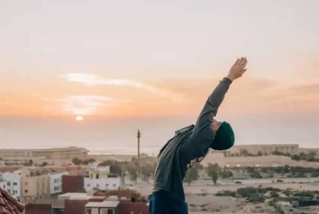 Yoga-Dehnung bei Sonnenuntergang auf einem Dach mit Blick über Tamraght und den Atlantik, Marokko