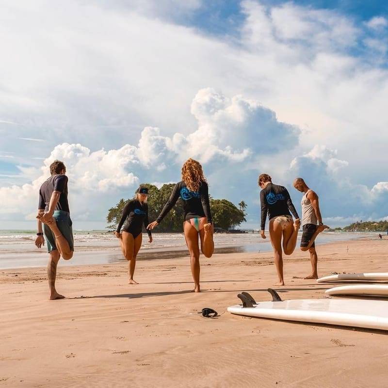 Gäste dehnen sich am Strand neben ihren Boards vor einer Surfsession in Weligama, Sri Lanka